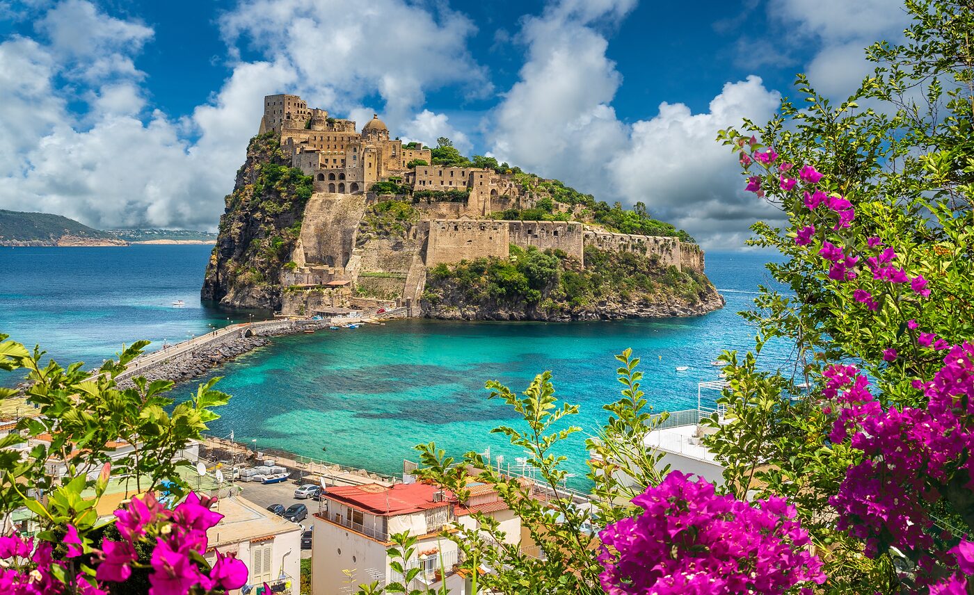 Aragonese Castle in Ischia rising above turquoise sea, framed by pink bougainvillea