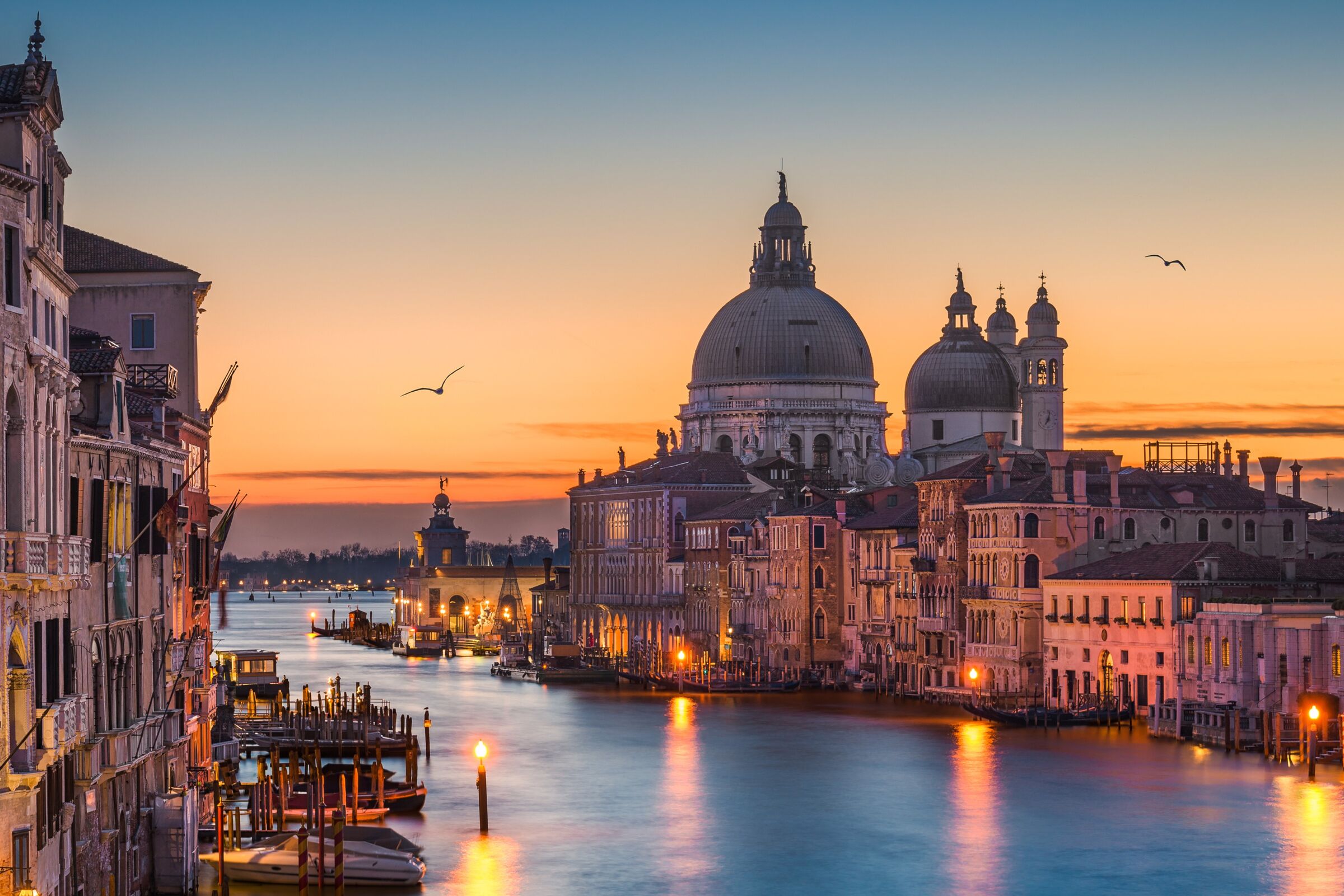 Grand Canal in Venice at dusk with the domes of Santa Maria della Salute against an orange sky