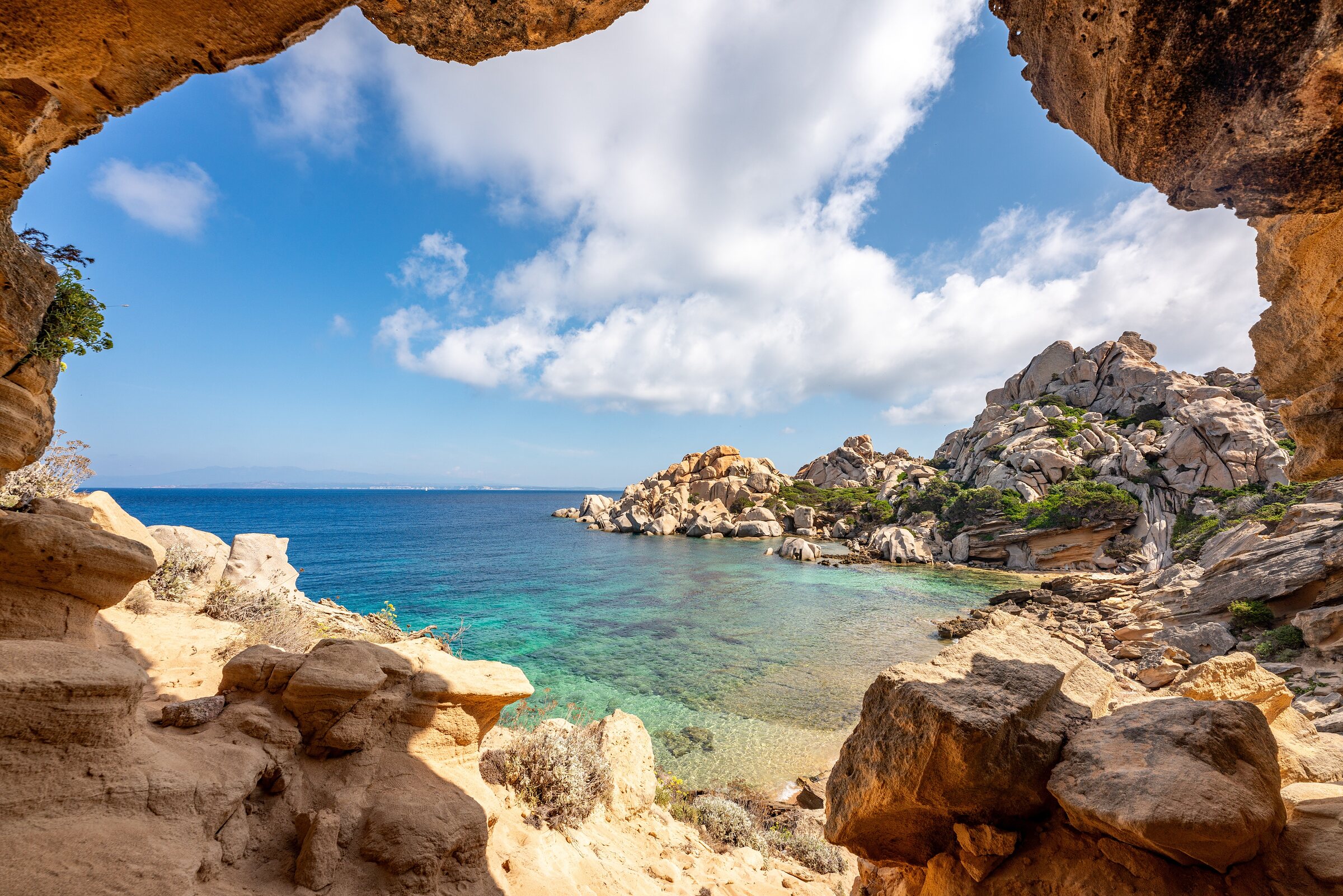 Turquoise cove and granite boulders in Sardinia, seen from inside a sandstone cave